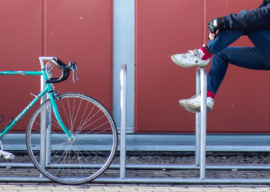 Una bicicletta e un ragazzo appoggiato ad alcune transenne